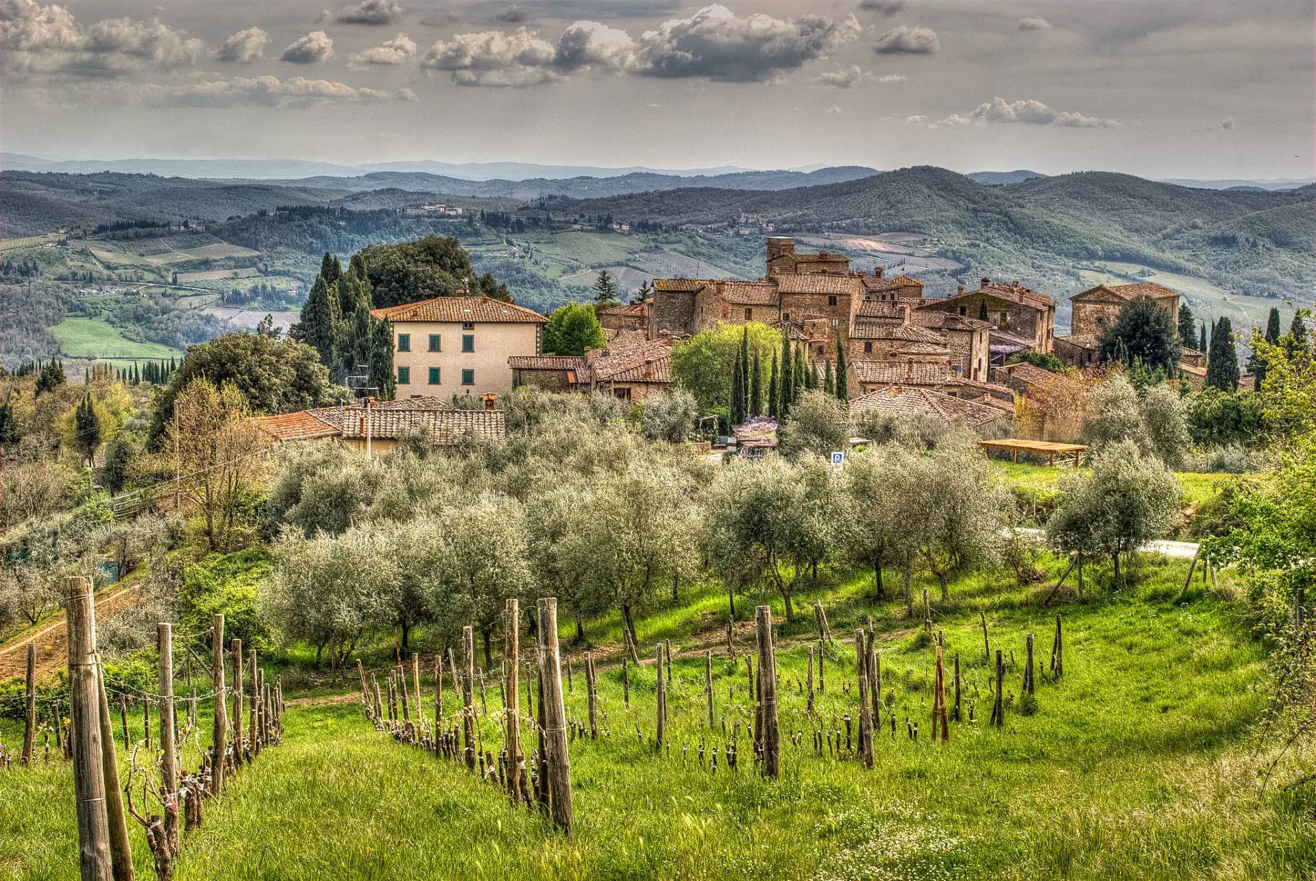 Vista panoramica di un borgo medievale del Chianti tra ulivi sotto un cielo drammatico