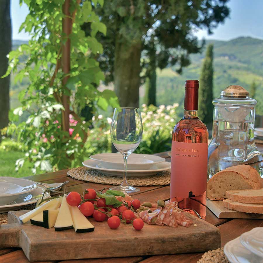 Tavola da pranzo all'aperto con vino rosé, formaggio, pomodori e pane in una cantina del Chianti