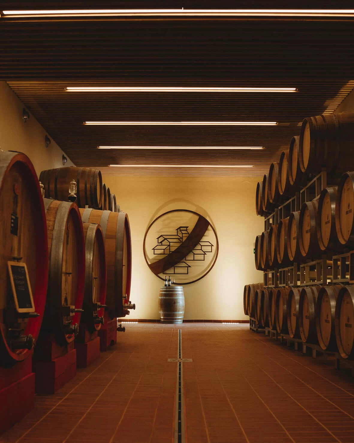 Cantina scenografica con file di grandi botti di rovere e stemma dell'azienda sulla parete