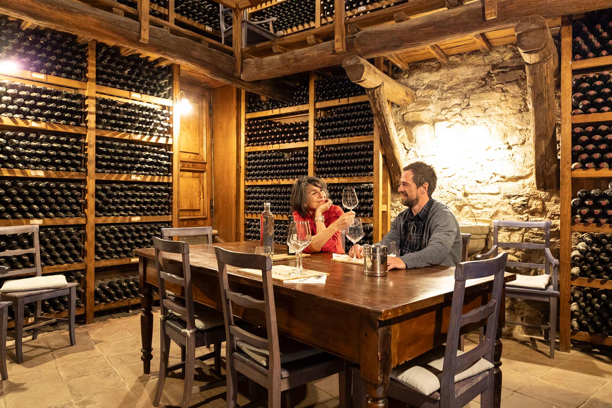 Una coppia degusta vino a un tavolo in una rustica cantina rivestita di bottiglie