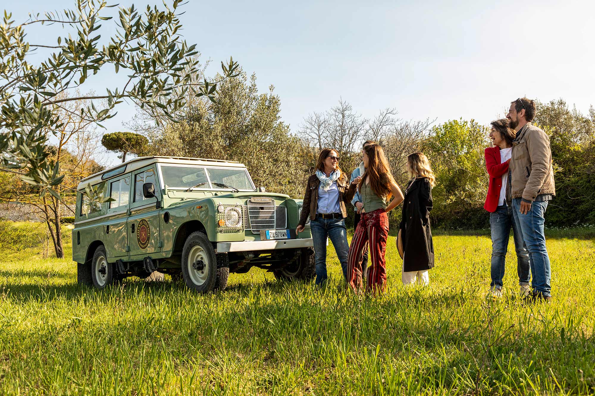 Ospiti riuniti attorno alla Land Rover in un uliveto mentre la guida spiega il territorio