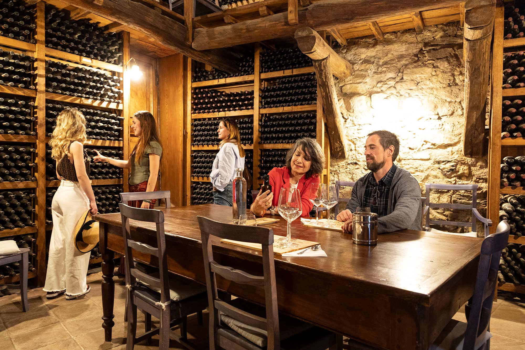 Gruppo di ospiti in degustazione in una rustica cantina in pietra rivestita di bottiglie