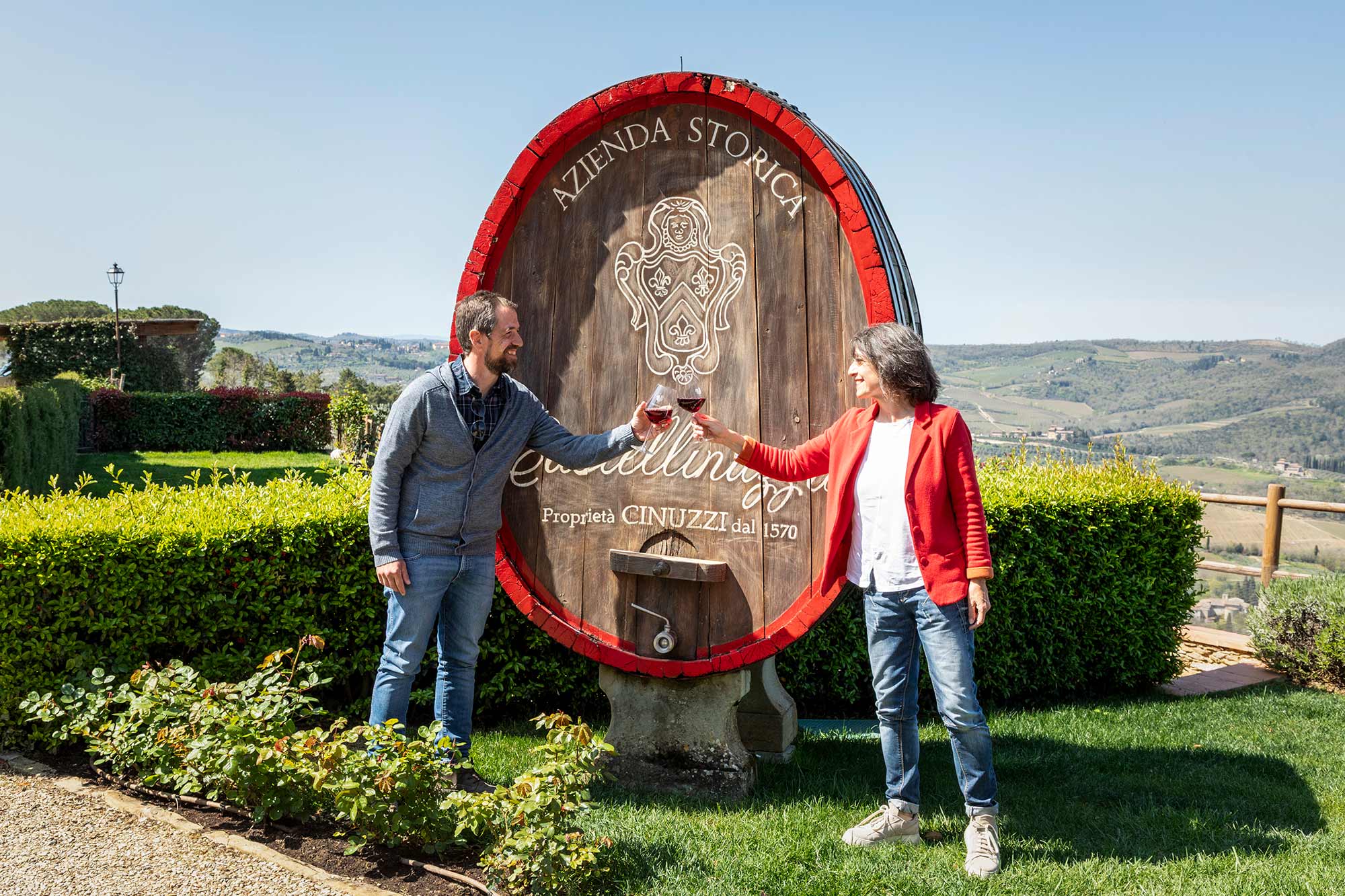 Una coppia brinda con calici di vino davanti alla grande botte con l'insegna Castellinuzzi